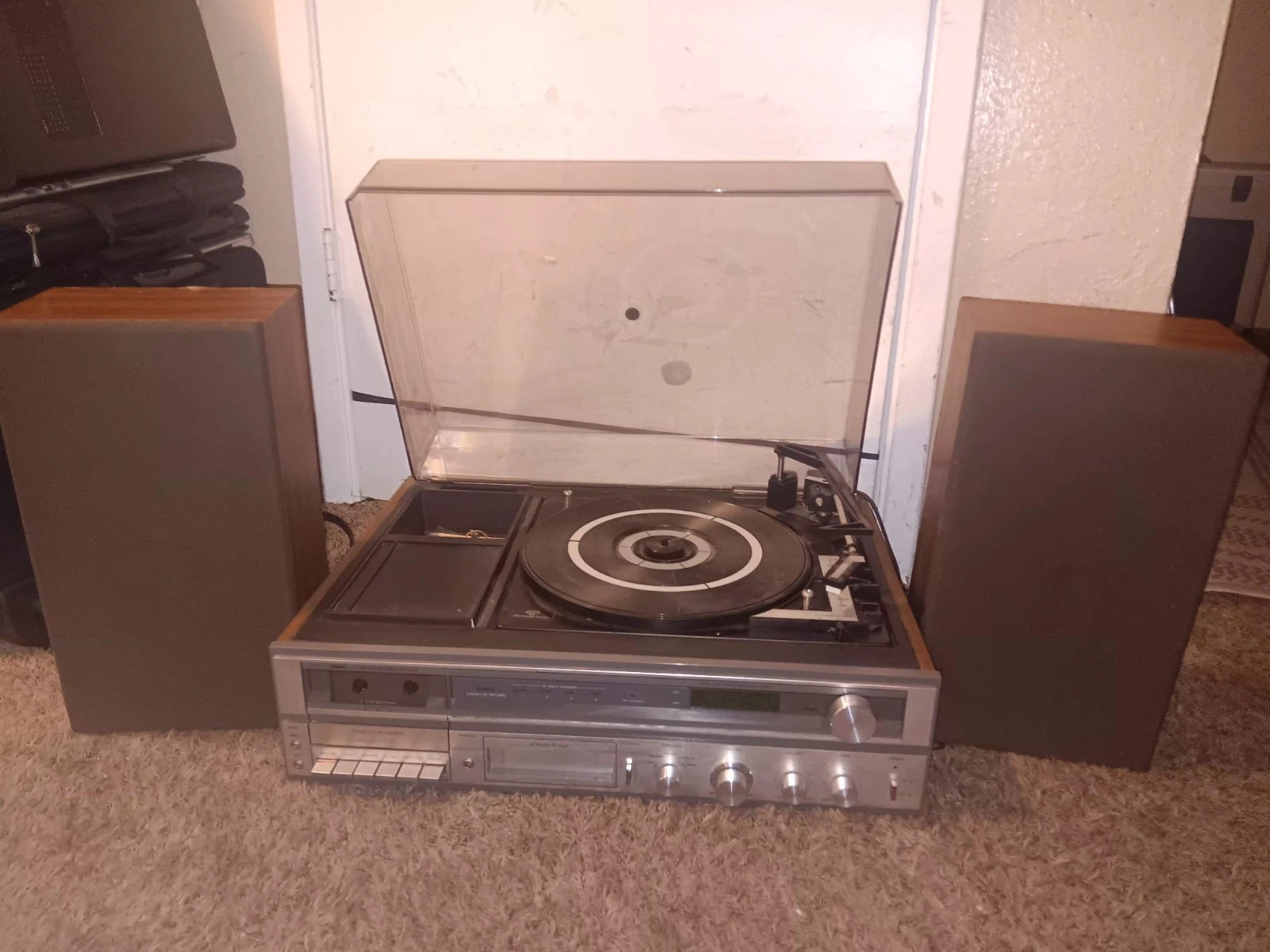 A Sears all-in-one stereo: turntable under a raised dust cover, cassette deck and 8-track slot below, flanked by two wood-cabinet speakers on shag carpet.